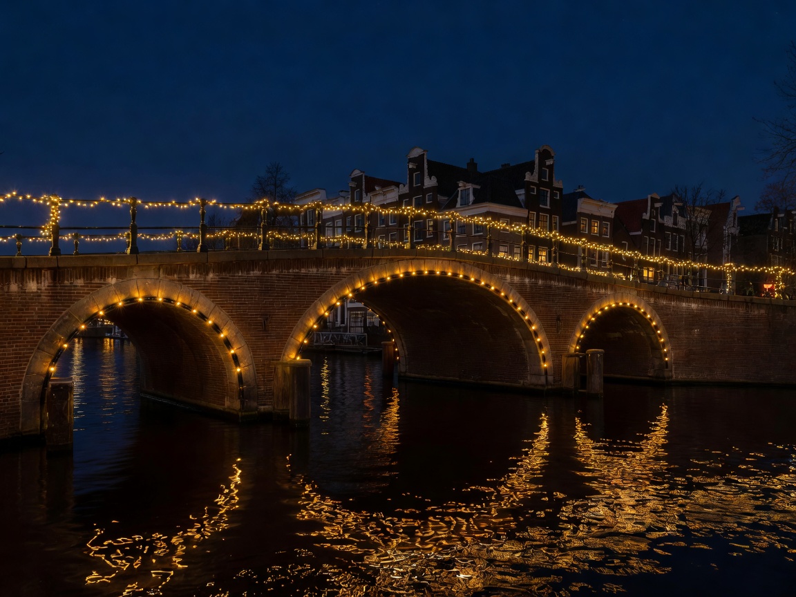 Amsterdam arched brick bridge lit with fairy lights reflecting in the dark canal water