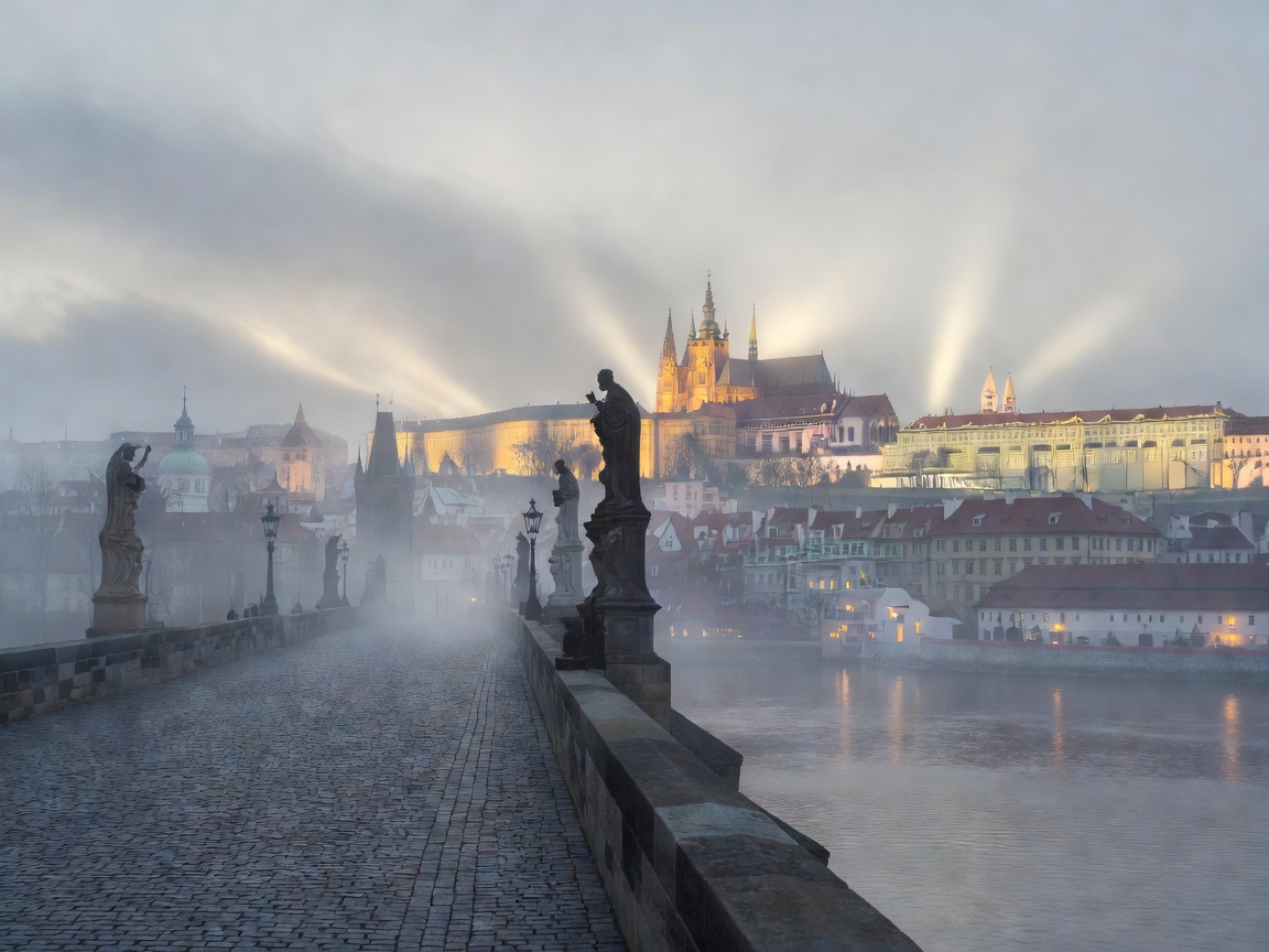 Charles Bridge in Prague shrouded in evening mist with illuminated castle in the background