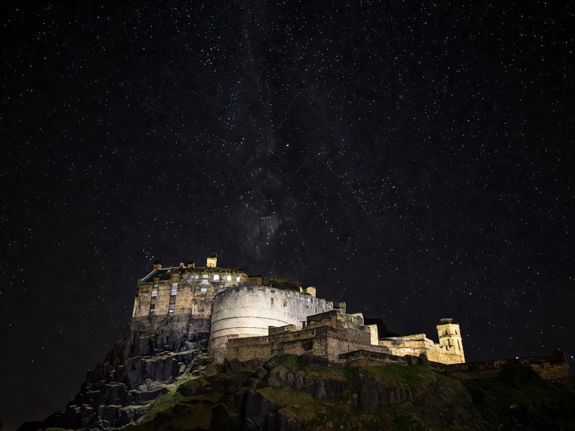 Edinburgh Castle perched high on illuminated volcanic rock under starry dark Scottish sky