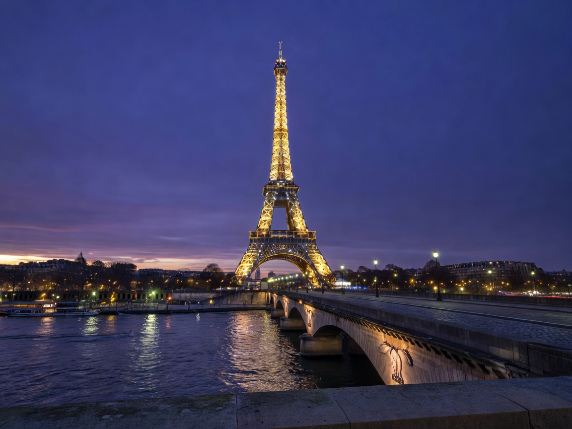 Eiffel Tower glittering against a deep twilight sky in Paris seen from the Seine bridge