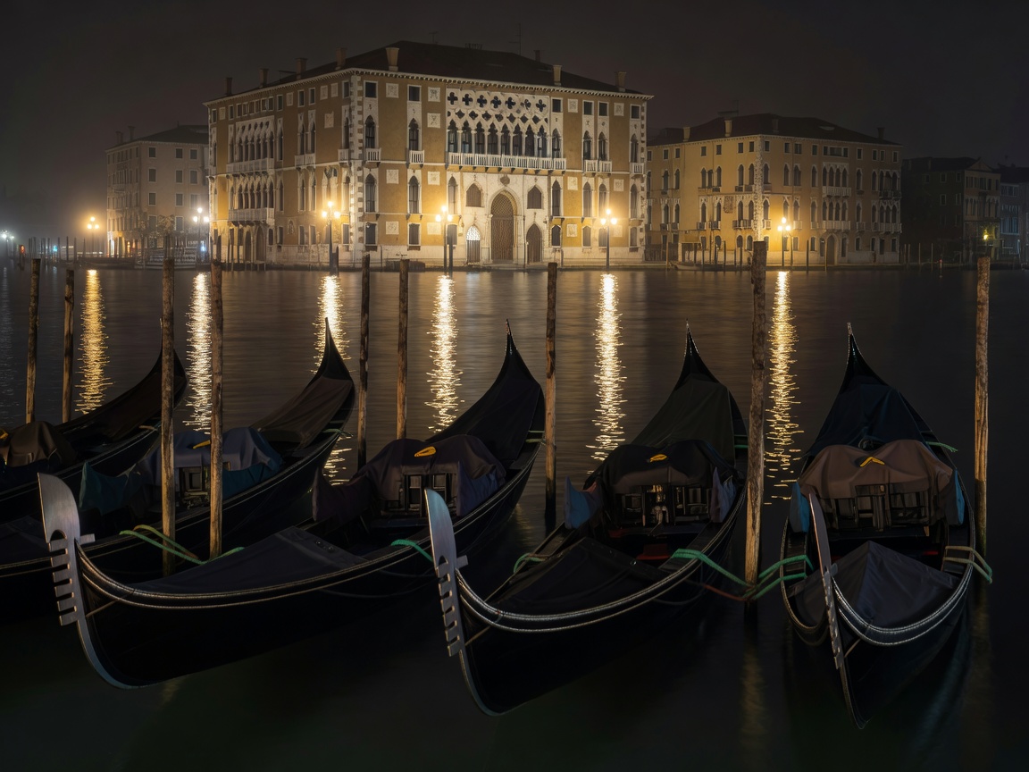Gondolas moored in dark lagoon water with distant illuminated Venetian palace lamps
