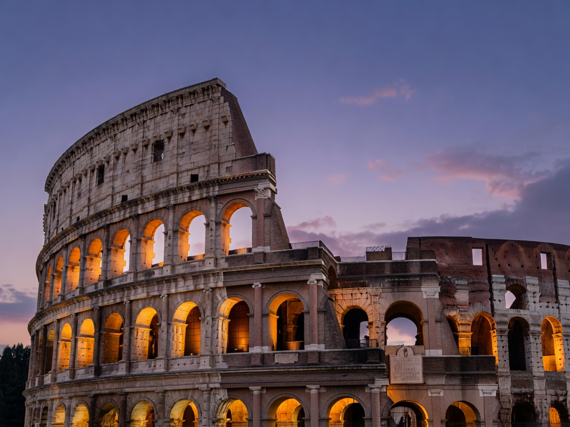 The Roman Colosseum illuminated from within inner arches with warm amber glow against twilight sky